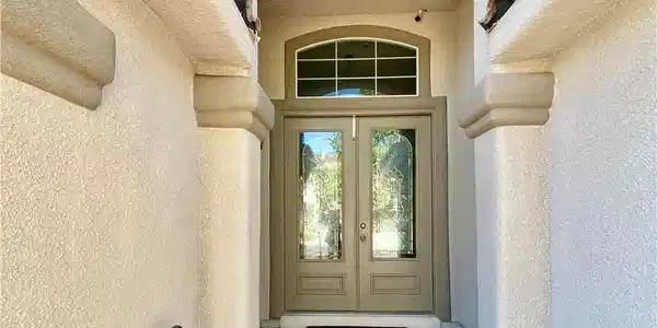 Image 3: An arched stucco entryway with glass-paneled doubl