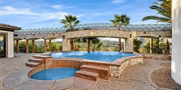 Image 3: An inviting pool and spa beckon with a stone bridg