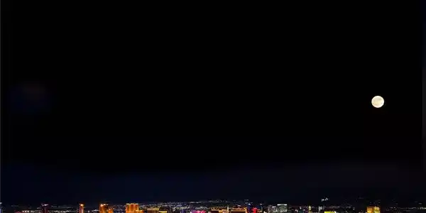 Image 3: City lights twinkle beneath a luminous full moon,