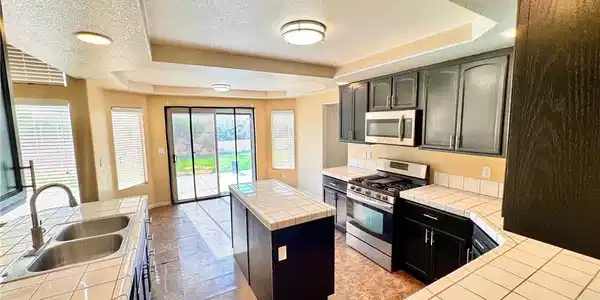 Image 4: A spacious kitchen features tile countertops, a ce
