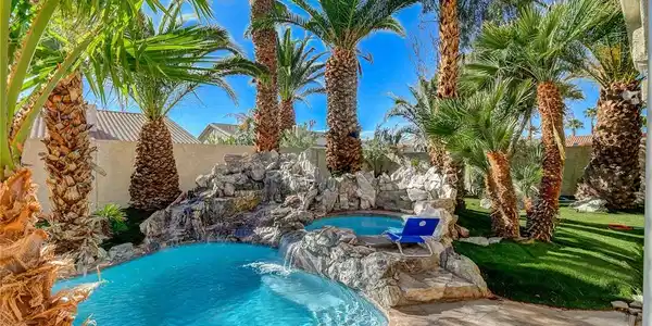 Image 4: Lush palm trees surround a custom rock waterfall p