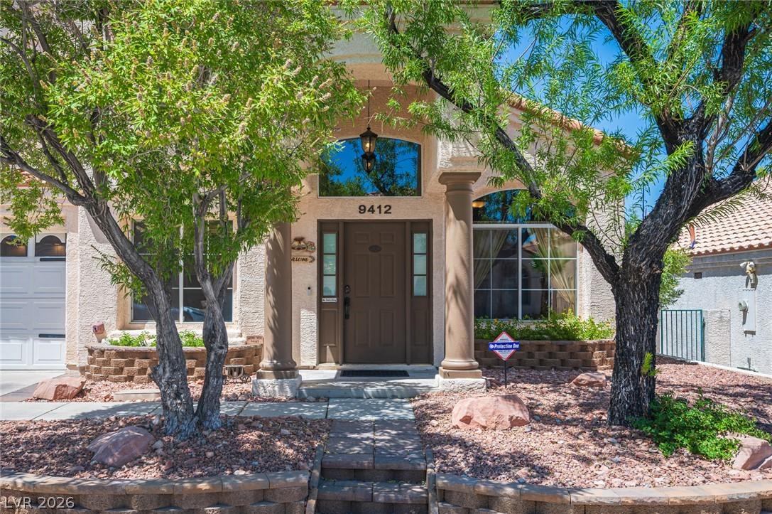 Image 2: A welcoming entry framed by lush trees and a stone