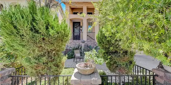 Image 4: Lush landscaping and a wrought iron fence frame th