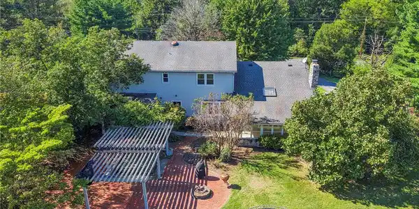 Image 4: Mature trees surround this home featuring a brick