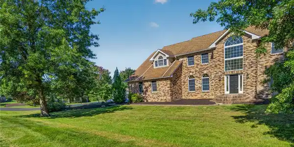 Image 3: Mature trees frame a classic brick multi-level hom