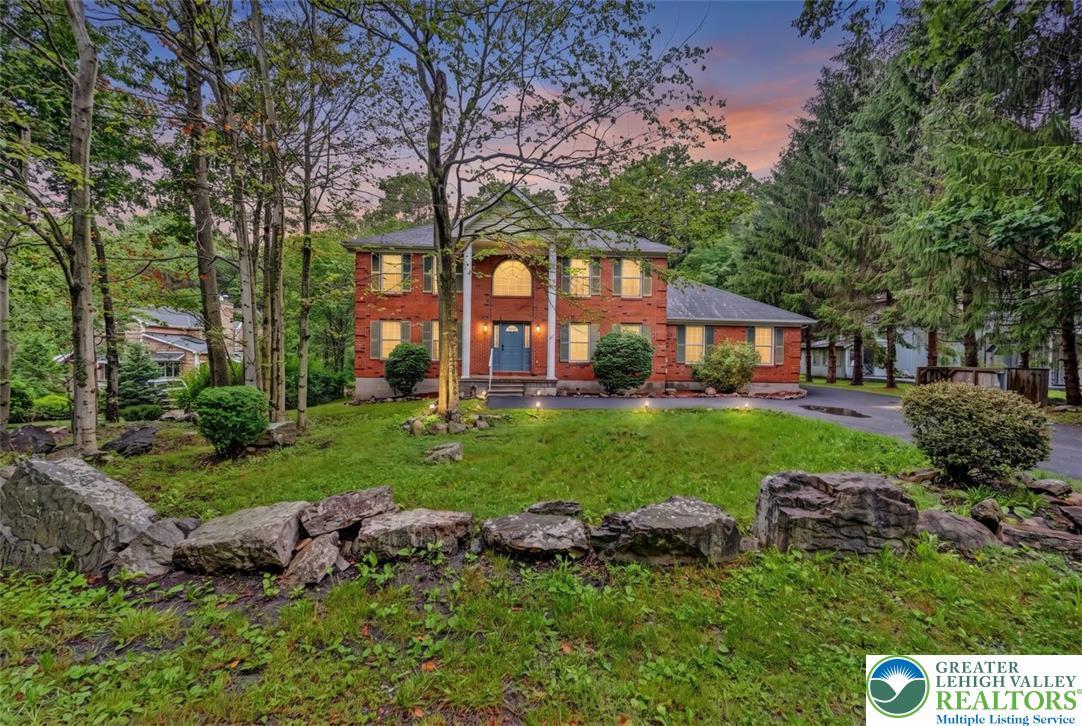 Image 2: Front Dusk Yard View. A stately brick home sits ma