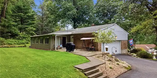 Image 2: Mature trees frame a classic brick and siding exte