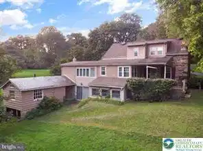 Image 2: Mature trees frame the stone and wood siding exter