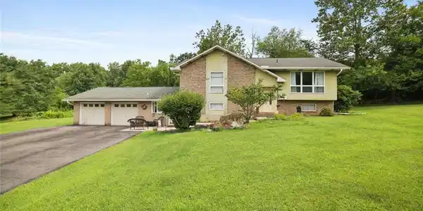 Image 2: Mature trees frame a classic brick and siding spli