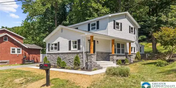Image 3: A welcoming facade showcases white siding, stone v