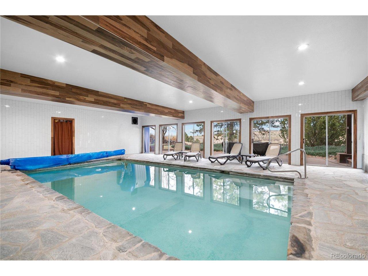 Image 2: Year-round heated indoor pool wrapped in stone flooring and walls of glass, offering natural light and direct access to outdoor living spaces.