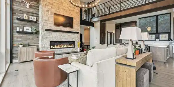 Image 3: Living area featuring light wood style flooring, a floor to ceiling stone fireplace, and vaulted ceilings.