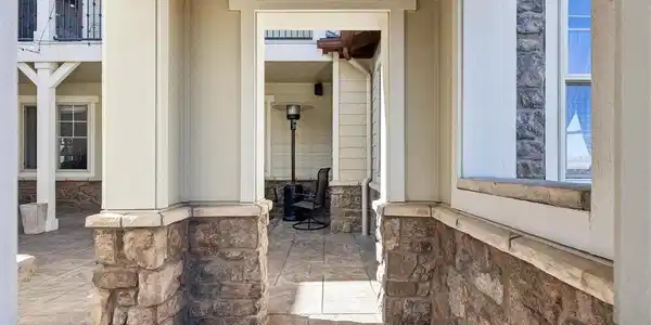 Image 2: Welcoming covered walkway with stone accents, architectural columns, and a sheltered approach into the home's private courtyard.