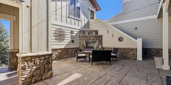 Image 3: Spacious stamped-concrete courtyard with stone accents, string lighting, a built-in outdoor fireplace, and a snow-melt system-an inviting setting for relaxing or entertaining in every season.