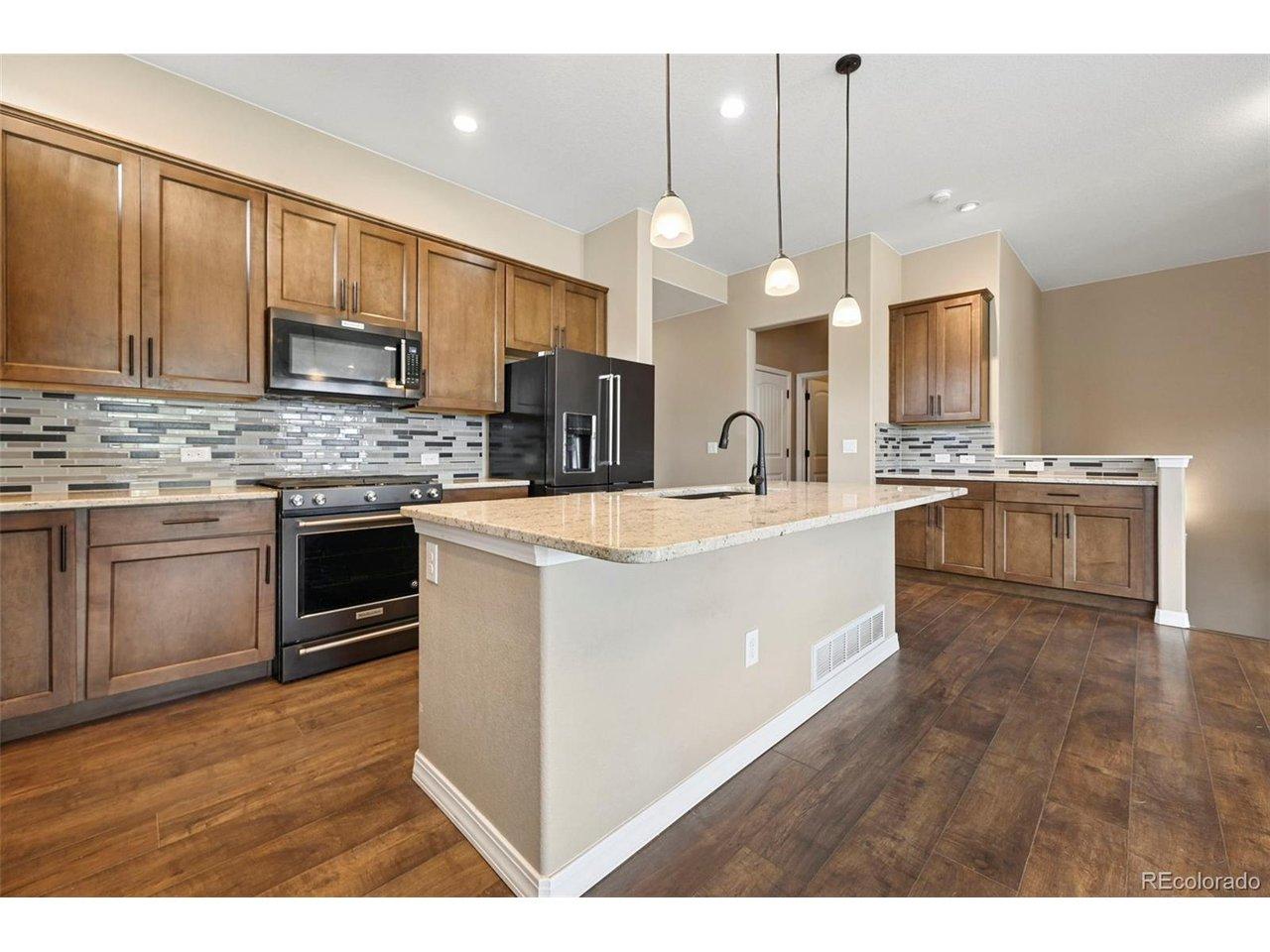 Image 4: Kitchen featuring wood-finish flooring, an oversized island with pendant lighting, stone countertops, a mosaic tile backsplash, and upgraded stainless steel appliances Image 4: Kitchen featuring wood-finish flooring, an oversized island with pendant lighting, stone countertops, a mosaic tile backsplash, and upgraded stainless steel appliances