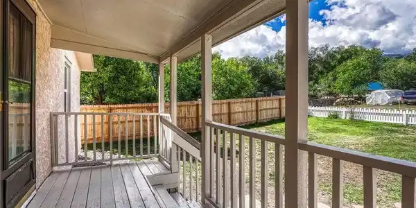 Image 3: Covered porch with wood-finish decking, solid wood railings, and a stucco exterior