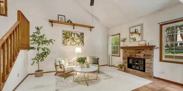 Image 4: Bright, inviting vaulted living room featuring neutral carpeting, a ceiling fan, wall shelf, & cozy wood-burning fireplace with a classic brick surround to cozy up on chilly evenings. Image 4: Bright, inviting vaulted living room featuring neutral carpeting, a ceiling fan, wall shelf, & cozy wood-burning fireplace with a classic brick surround to cozy up on chilly evenings.