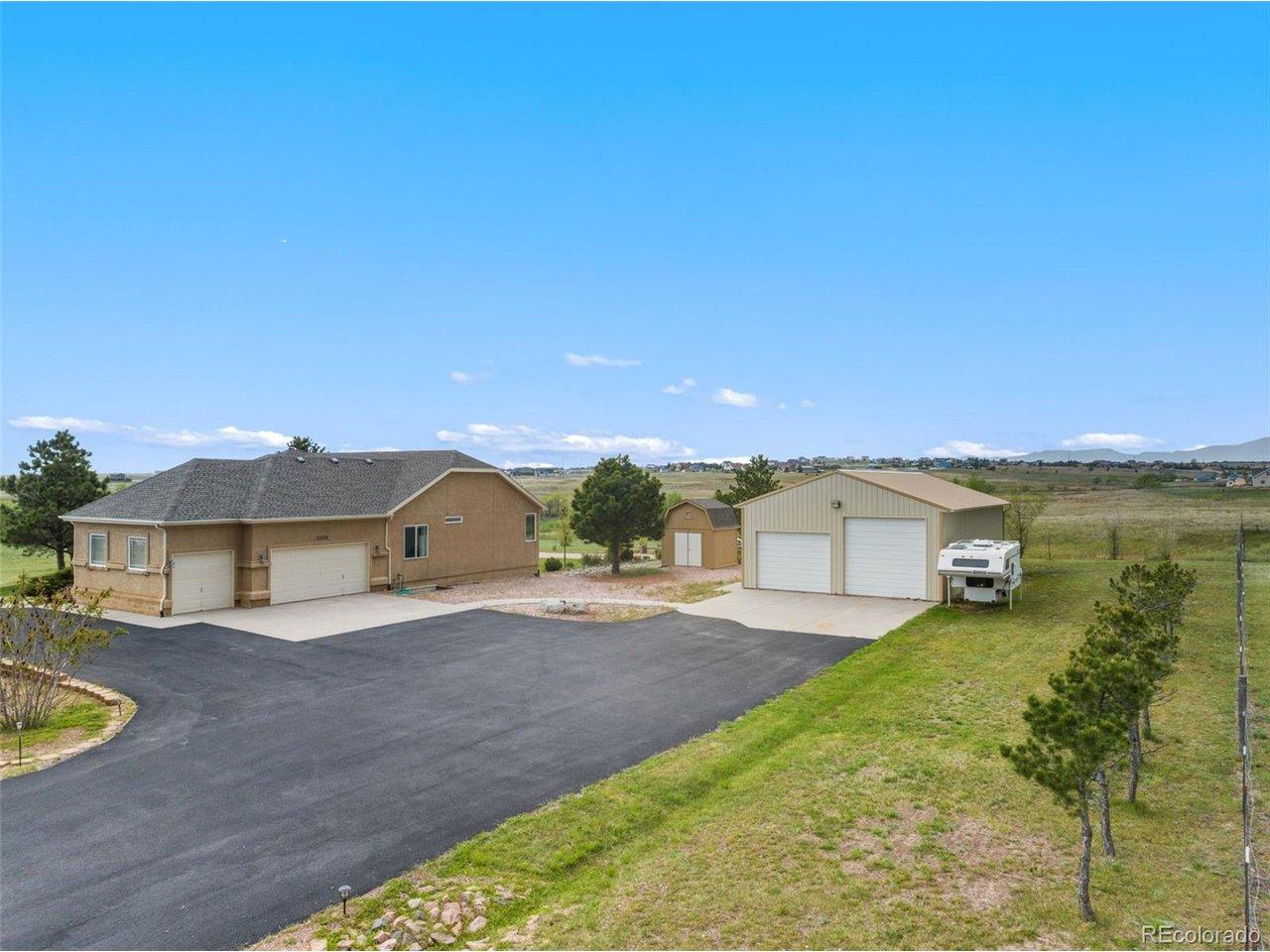 Image 2: Side entry of home with asphalt driveway, 3-car attached garage, small shed and large shop with RV garage door.