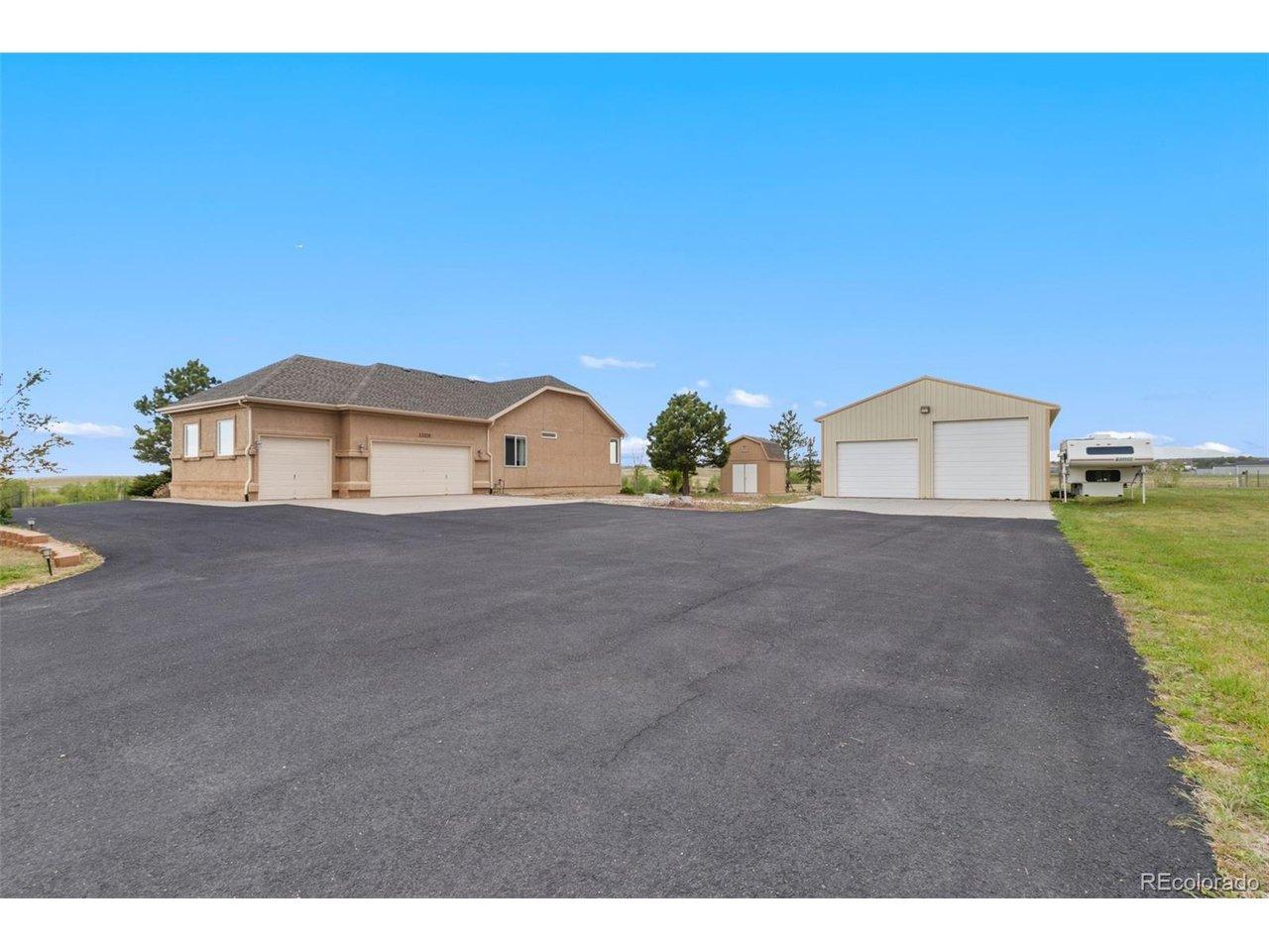 Image 3: Side entry of home with asphalt driveway, 3-car attached garage, small shed and large shop with RV garage door.
