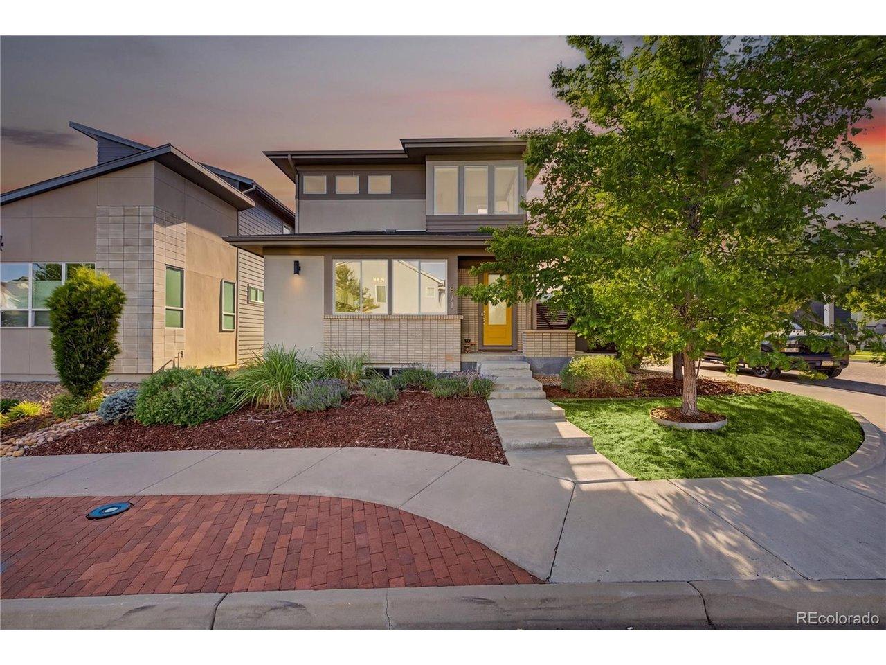 Image 1: Stunning contemporary two-story home with stucco and brick exterior, bold yellow front door, mature shade tree, and meticulously landscaped front yard featuring drought-tolerant plantings, decorative mulch beds, and a charming brick-paver driveway apron.