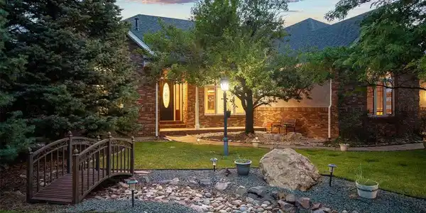 Image 3: Welcoming front entrance framed by mature trees, lush landscaping, and a charming footbridge. Image 3: Welcoming front entrance framed by mature trees, lush landscaping, and a charming footbridge.