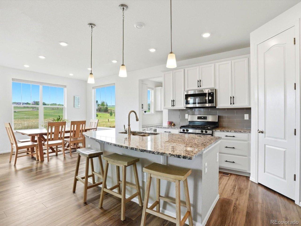 Image 3: Chef-inspired kitchen featuring a large granite island with seating, stainless steel appliances, white cabinetry, and breathtaking Colorado views from every window Image 3: Chef-inspired kitchen featuring a large granite island with seating, stainless steel appliances, white cabinetry, and breathtaking Colorado views from every window