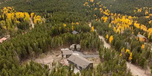 Image 2: Tucked into a sea of green pines and golden aspens, this home doesn't just sit in the mountains - it disappears into them. Two flat acres of privacy, framed by a hillside that turns to gold every autumn. This is the kind of setting people move to Evergreen