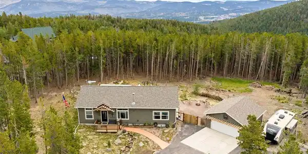 Image 4: Front porch, detached garage, and mountains stacking up behind - this is the whole package from above. Flat, usable acreage means room to roam, room to build, room to just breathe, with the Rockies standing watch on the horizon.
