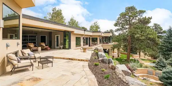 Image 2: An expansive flagstone patio flows seamlessly from the interior through walls of glass, offering comfortable lounge seating and lush rock-garden landscaping.