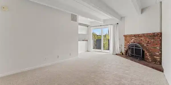 Image 3: Bright living area with brand-new carpet, fresh paint, exposed ceiling beams, and a wood-burning fireplace. Image 3: Bright living area with brand-new carpet, fresh paint, exposed ceiling beams, and a wood-burning fireplace.