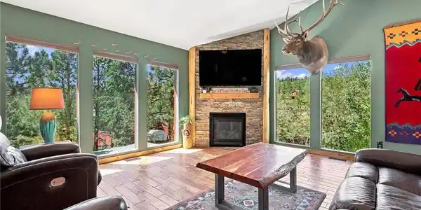 Image 4: The sun-drenched, open-concept main level living room features dramatic vaulted ceilings, a cozy stone-clad fireplace, and massive walls of windows. Image 4: The sun-drenched, open-concept main level living room features dramatic vaulted ceilings, a cozy stone-clad fireplace, and massive walls of windows.