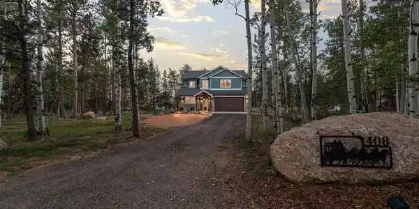 Image 4: The journey home is half the magic - a winding gravel drive framed by towering aspens, leading you toward a house that glows like a beacon in the trees. The custom stagecoach address marker offers a nod to the road's namesake as you arrive at your private