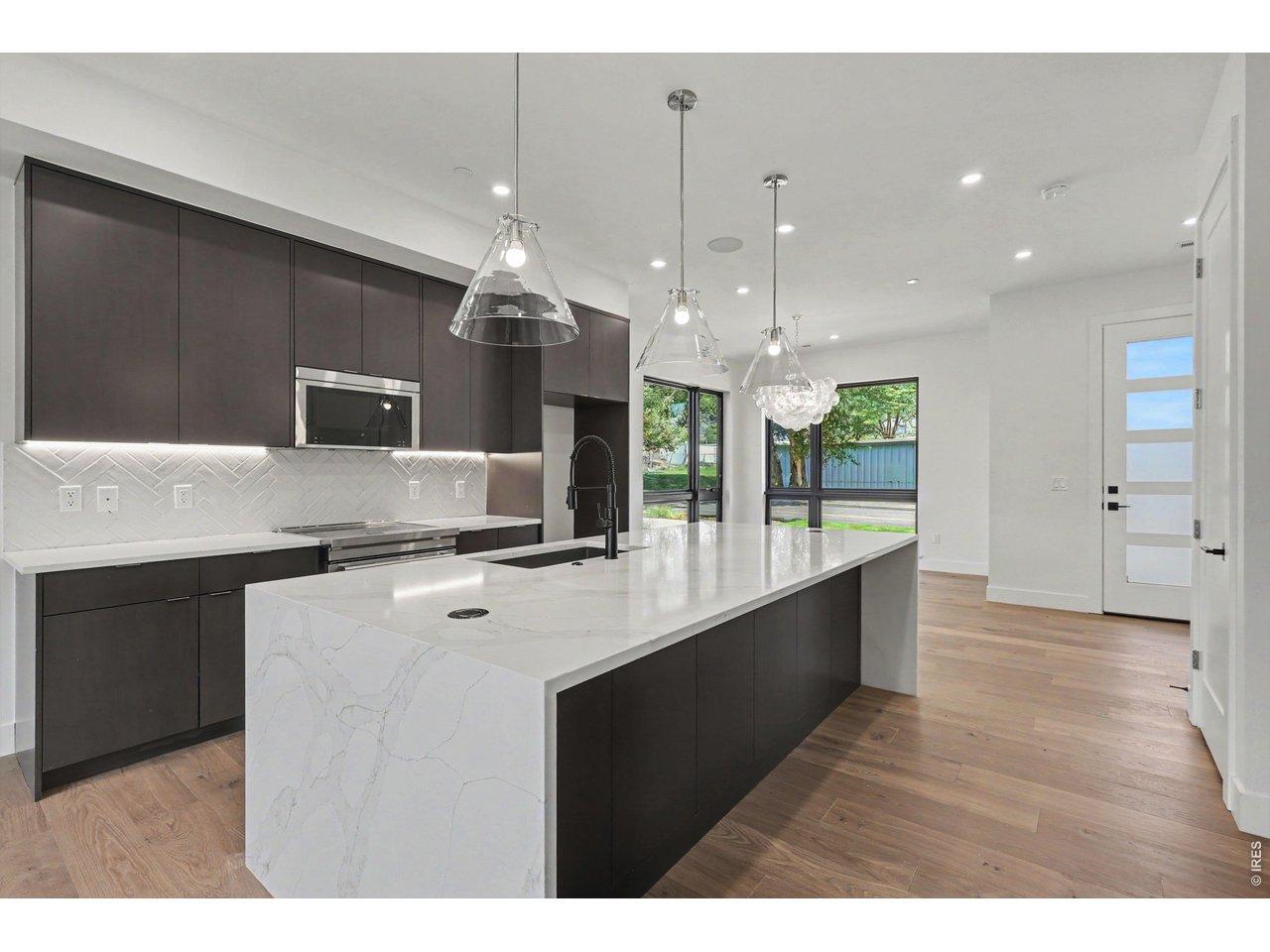 Image 4: At the heart of the home, the chef's kitchen showcases a dramatic waterfall-edge quartz island, custom cabinetry, premium JennAir appliances, designer lighting, and generous prep space designed for everyday living and effortless entertaining.