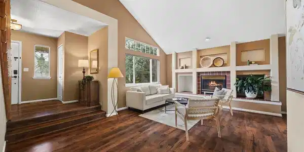 Image 3: Dramatic vaulted living room with rich wood-look flooring, oversized windows, built-in shelving, and a gas fireplace anchoring the space. Image 3: Dramatic vaulted living room with rich wood-look flooring, oversized windows, built-in shelving, and a gas fireplace anchoring the space.
