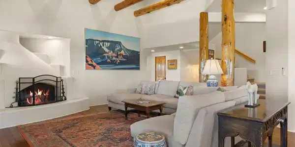 Image 4: The great room showcases a 14-foot ceiling with hand-hewn log beams, natural column supports, and a kiva-style wood-burning fireplace framed by a traditional banco bench. Image 4: The great room showcases a 14-foot ceiling with hand-hewn log beams, natural column supports, and a kiva-style wood-burning fireplace framed by a traditional banco bench.