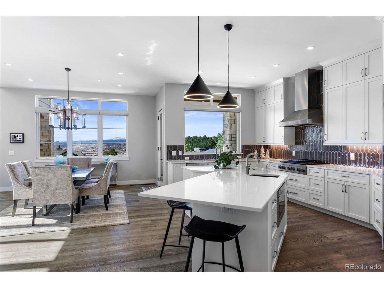 Image 4: Kitchen with quartz countertops, center island, Dacor and Sharps appliances, floor-to-ceiling white cabinetry, stylish tile backsplash, and open flow to the dining area.