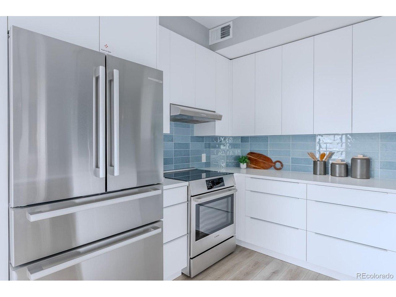 Image 4: Stainless Bosch appliances, complemented by an induction range with an exterior vent hood for a clean cooking experience, lend both performance and polish, and a soft tile backsplash introduces a gentle layer of texture. Image 4: Stainless Bosch appliances, complemented by an induction range with an exterior vent hood for a clean cooking experience, lend both performance and polish, and a soft tile backsplash introduces a gentle layer of texture.