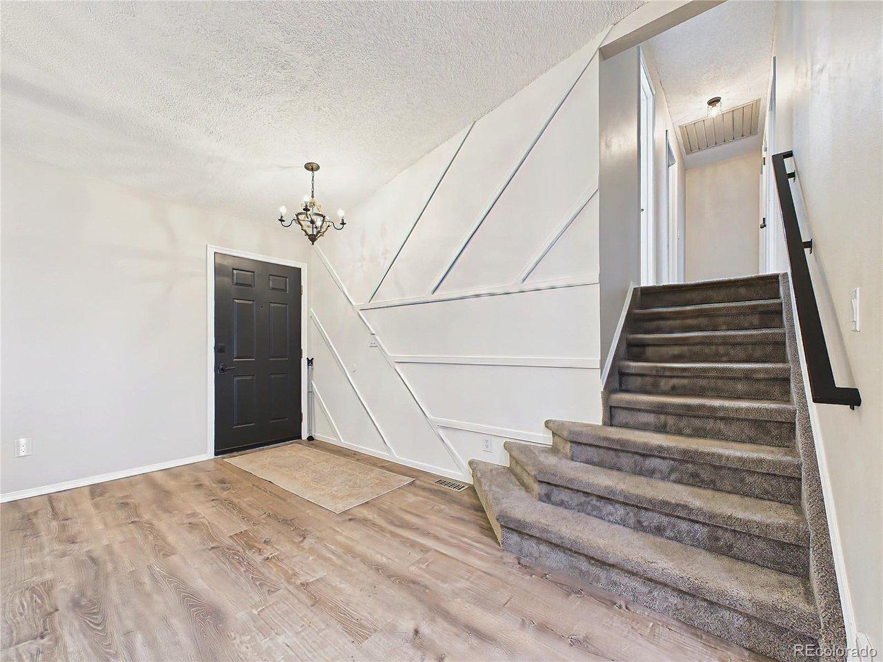 Image 4: Welcoming entry with updated luxury vinyl plank flooring, modern black front door, decorative accent wall, and an open staircase creating a stylish first impression. Image 4: Welcoming entry with updated luxury vinyl plank flooring, modern black front door, decorative accent wall, and an open staircase creating a stylish first impression.