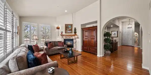 Image 3: Open great room with two-sided gas fireplace with a stone surround, wood floors, and an archway view into the foyer beyond. Image 3: Open great room with two-sided gas fireplace with a stone surround, wood floors, and an archway view into the foyer beyond.
