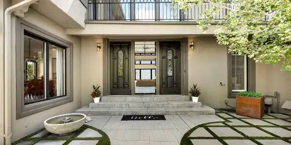 Image 2: The paver courtyard sets the tone before the front door opens. A checkerboard grid of stone and turf, the circular gate motif, and mature aspens signal immediately that this home operates at a different level.