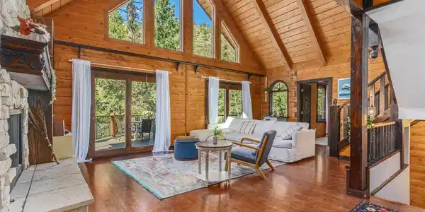 Image 4: Oh, the light! This living room is dreamy with two doors to the deck, soaring wood paneled ceilign and stone fireplace