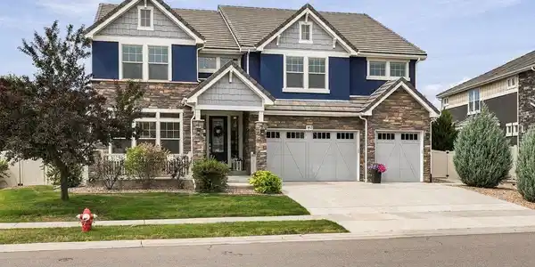 Image 3: The Blue House by day beautifully maintained landscaping, stone details and a three-car garage. Image 3: The Blue House by day beautifully maintained landscaping, stone details and a three-car garage.