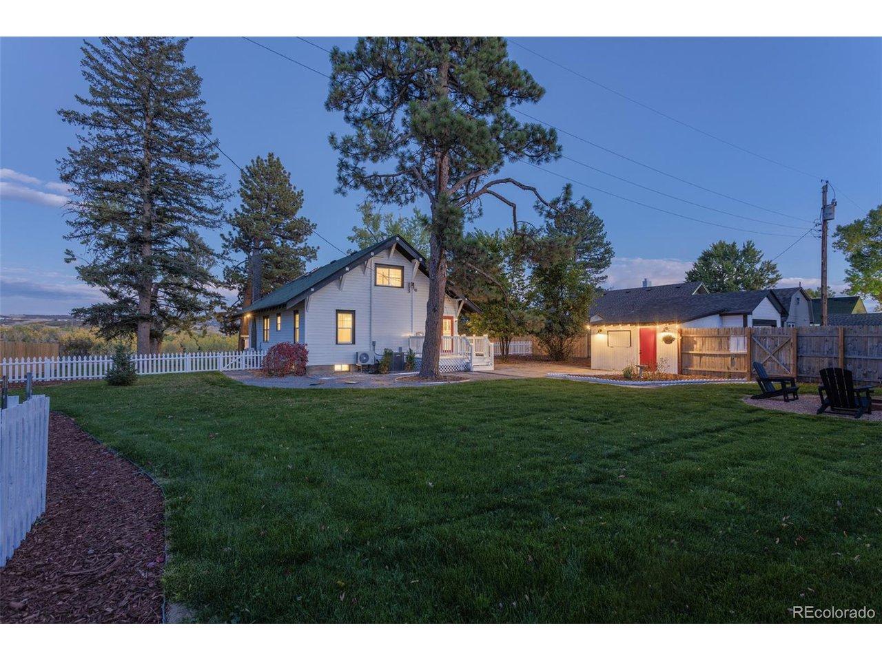 Image 2: Generous, Private Grounds. Enjoy the spacious, meticulously manicured lawn, framed by a classic white picket fence and mature trees. This expansive yard provides the perfect setting for recreation, entertaining, and private enjoyment. Backyard and back of
