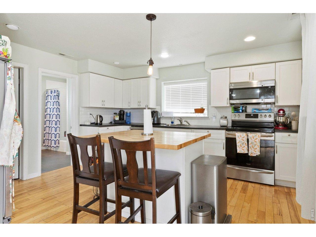 Image 2: The kitchen showcases whitewashed cabinetry, upgraded appliances, subway tile backsplash, and a large butcher block island with seating.
