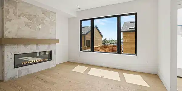 Image 2: Light-filled living room anchored by a sleek electric fireplace with custom tile surround & expansive windows.