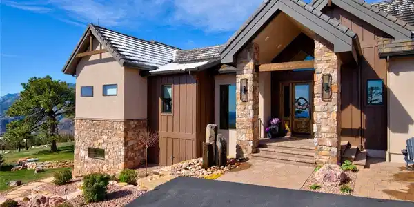 Image 3: Welcome home. Distinctive front elevation showcasing custom stone columns, board-and-batten siding, knotty alder double doors, and a tranquil basalt water feature at the entry.