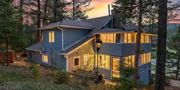 Image 4: From this angle, the home's sprawling footprint and craftsman details truly shine - a stone chimney, warm shingled siding, and windows glowing gold against the fading sky. Nestled into the hillside with a peek of water in the distance, this is mountain liv Image 4: From this angle, the home's sprawling footprint and craftsman details truly shine - a stone chimney, warm shingled siding, and windows glowing gold against the fading sky. Nestled into the hillside with a peek of water in the distance, this is mountain liv