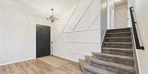 Image 4: Welcoming entry with updated luxury vinyl plank flooring, modern black front door, decorative accent wall, and an open staircase creating a stylish first impression. Image 4: Welcoming entry with updated luxury vinyl plank flooring, modern black front door, decorative accent wall, and an open staircase creating a stylish first impression.