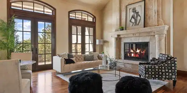 Image 3: Great room with soaring ceilings, a floor-to-ceiling carved stone fireplace, wide-plank walnut floors, and French doors opening to the terrace.