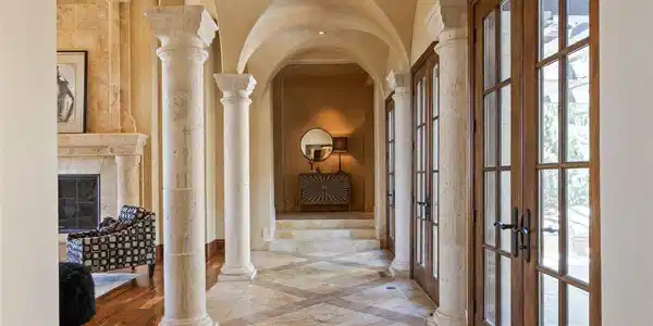 Image 4: Arched hallway with stone columns, travertine flooring, and multiple sets of French doors.